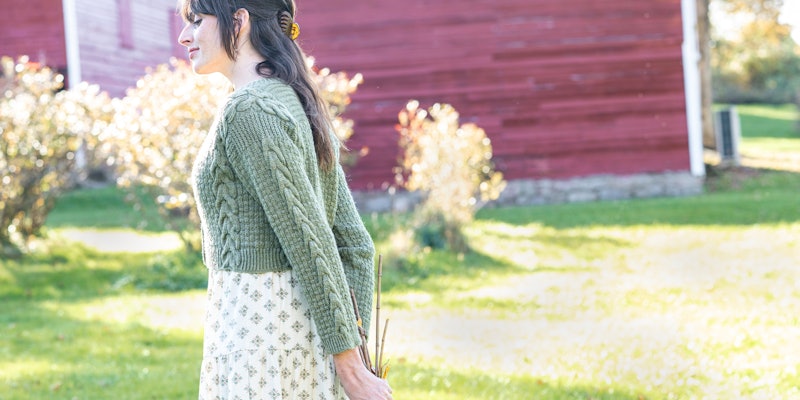 Woman in sage-green cardigan and flowered dress, holding dried flowers