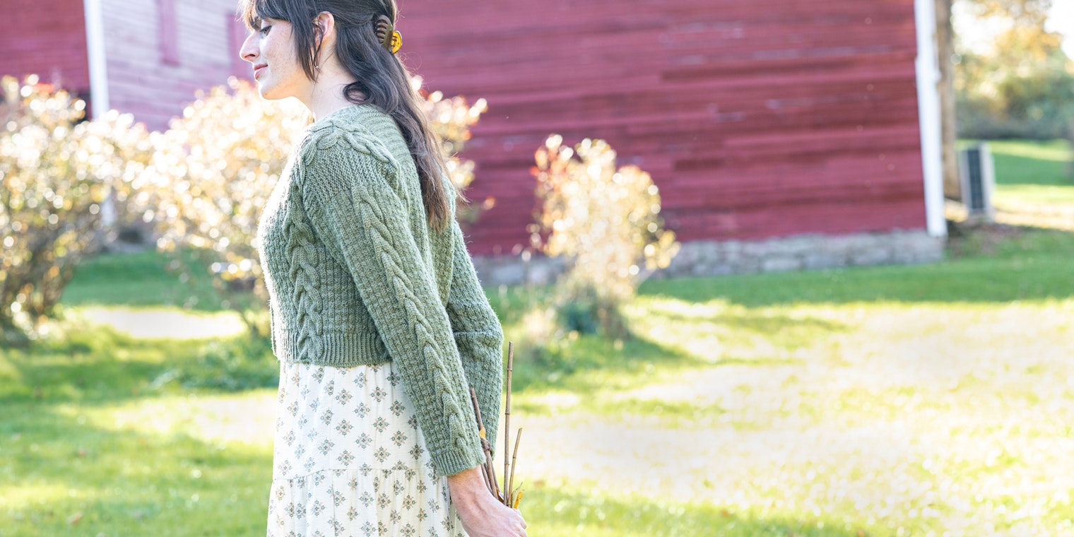 Woman in sage-green cardigan and flowered dress, holding dried flowers
