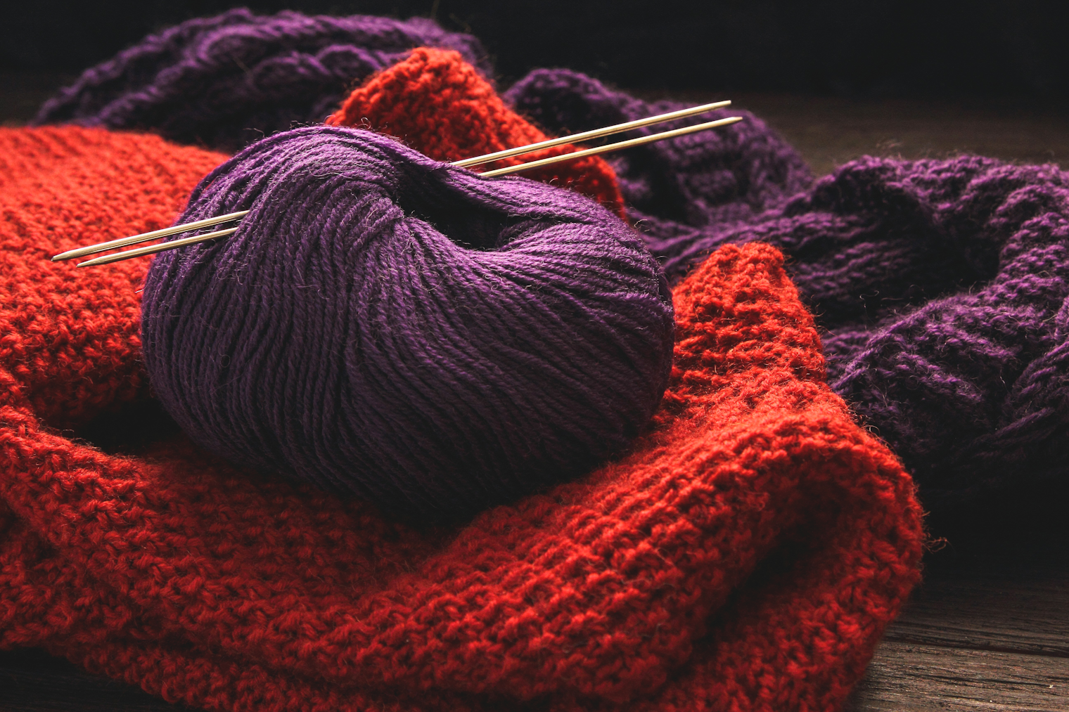 purple yarn with knitting needles on red and purple knitted garments