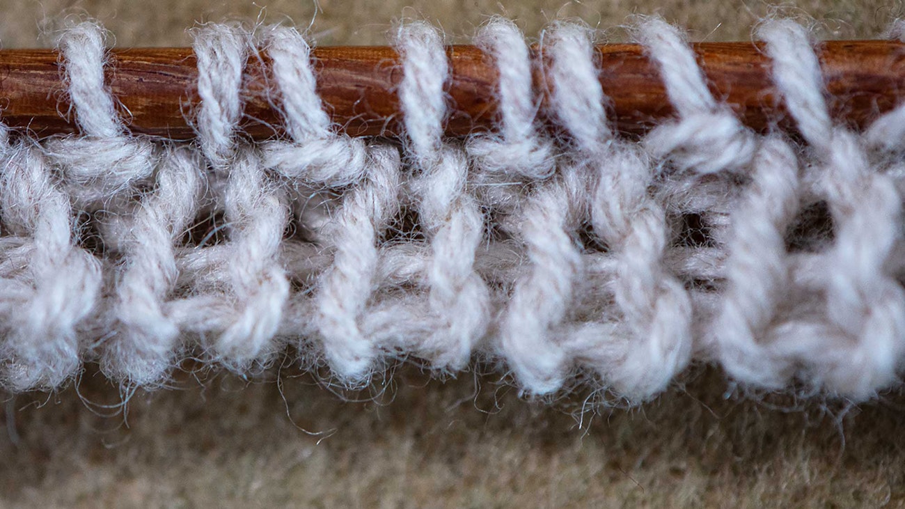 A close-up image of a long-tail tubular cast-on edge of gray knitting resting on a tan background.