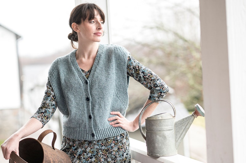 woman in a sage green vest with watering can