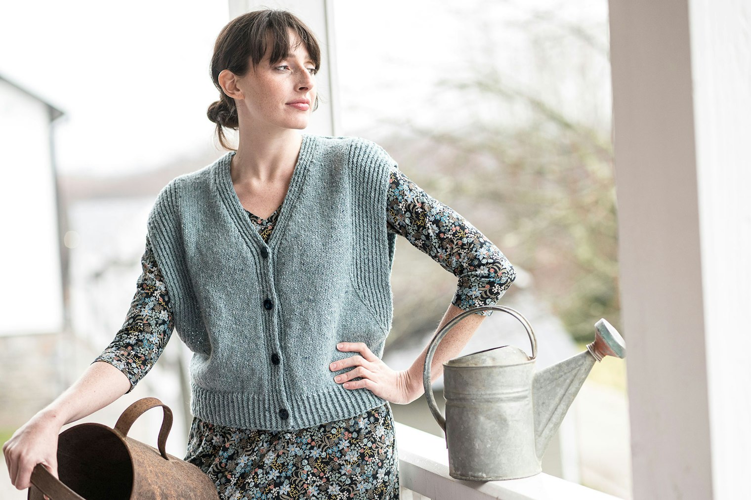 woman in a sage green vest with watering can