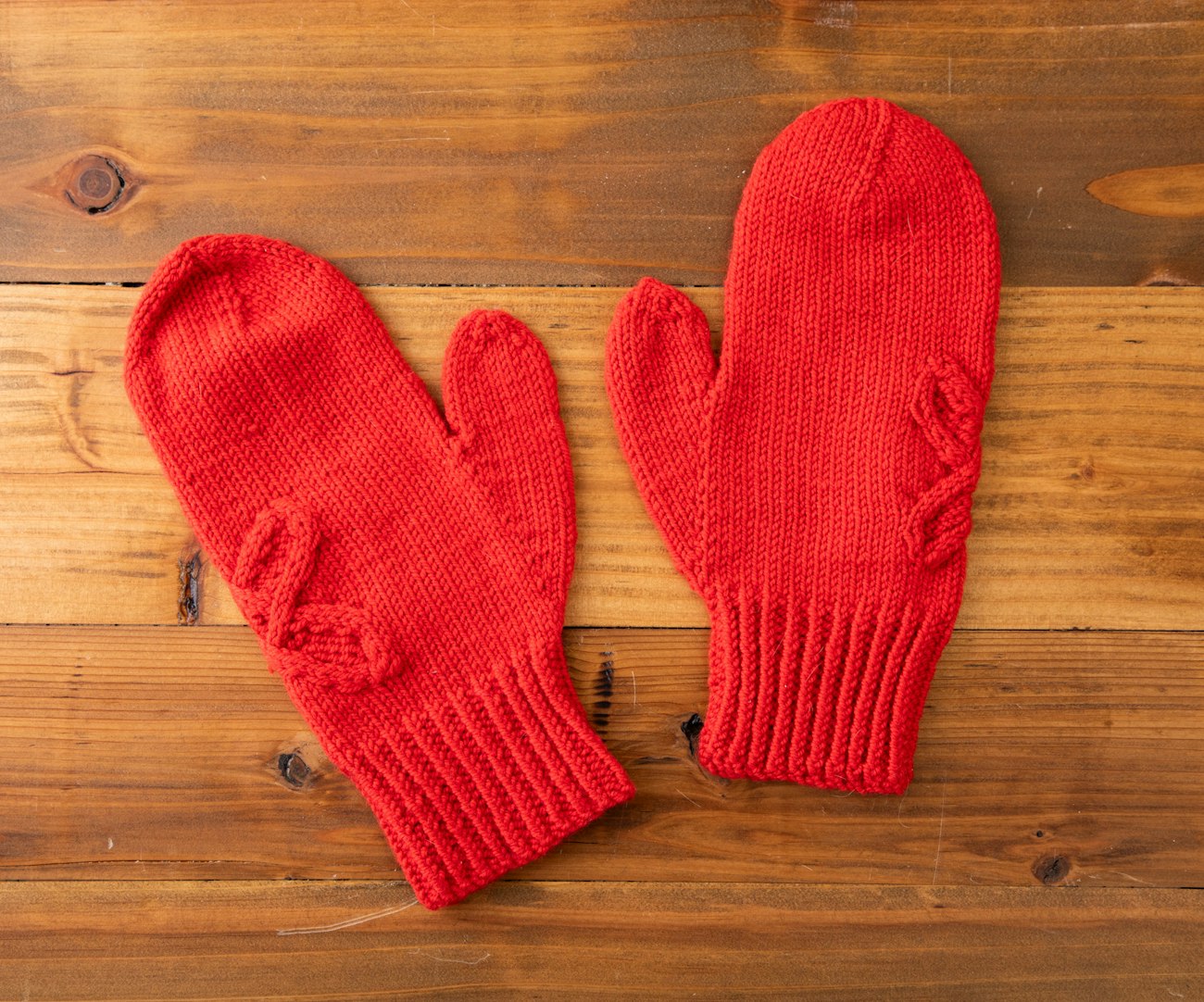 Two red mittens on a brown wool table