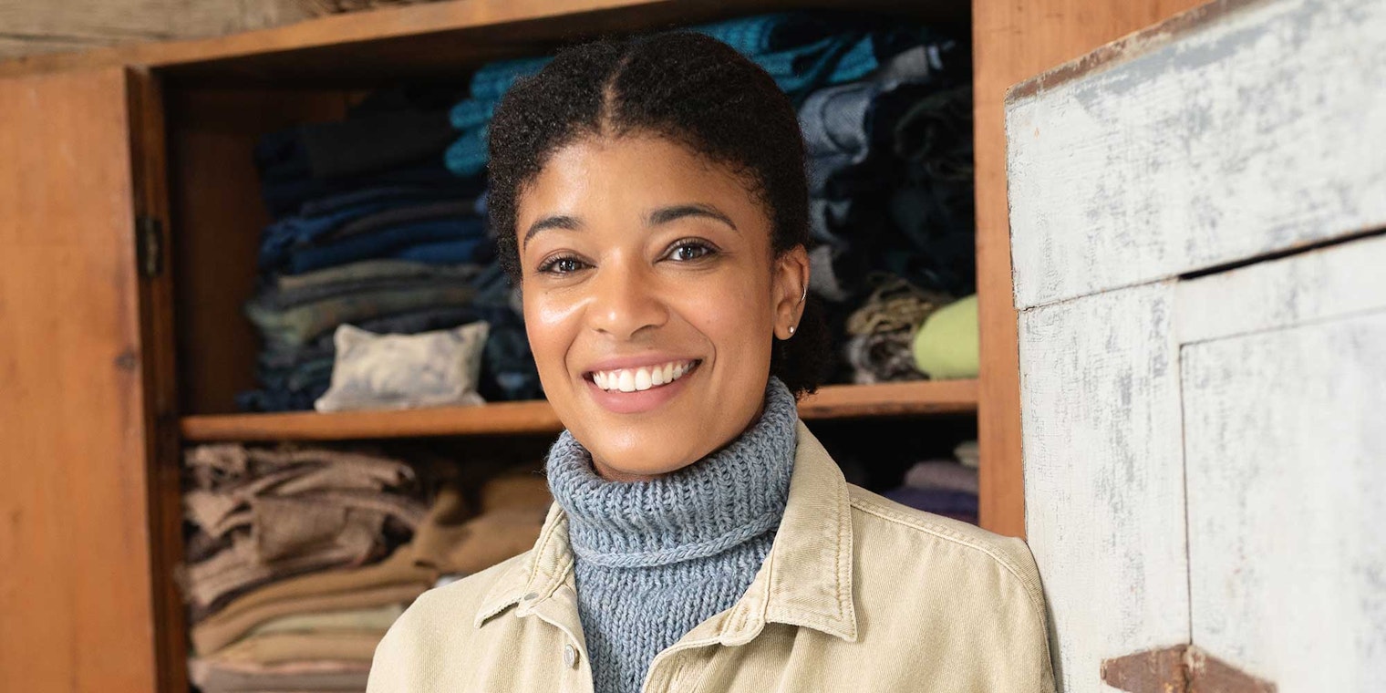 A woman stands in front of a wardrobe, wearing a neckwarmer.