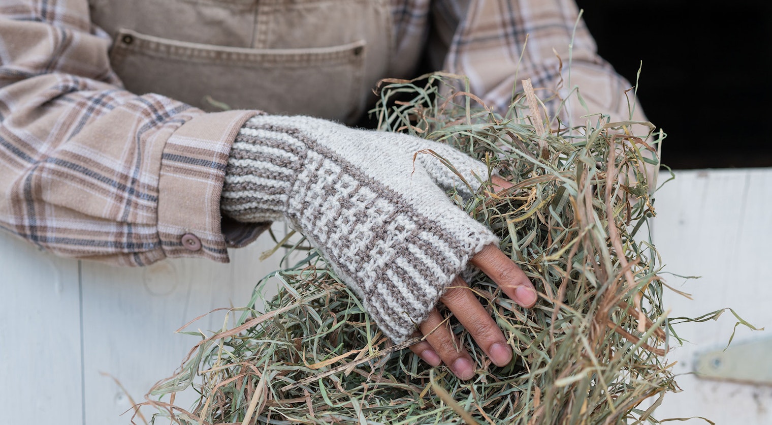 beige and white knitted mitts on hands holding hay