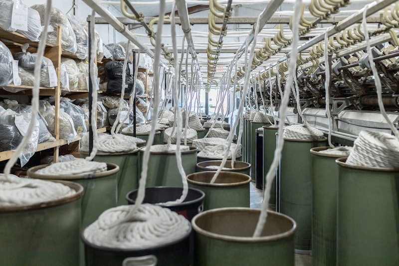 At left, a wall of shelves holds wool coming in to be processed. At center, bins of pindrafted roving wait to be pulled onto the spinning frame at right. Photo by Ash Patiño/Generic Brand Human