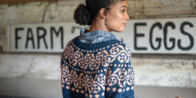 A woman wearing a floral yoke pullover collects eggs on a farm.