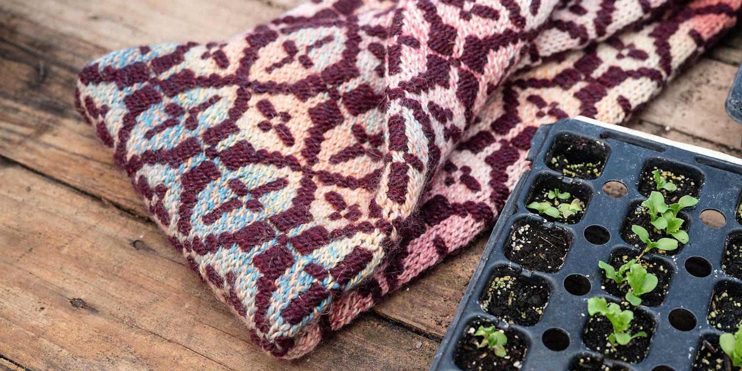 A colorwork cowl rests on a wooden surface with a tray of seedlings.