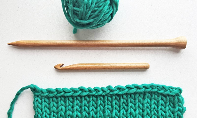 ball of green yarn, tools, and knitted swatch