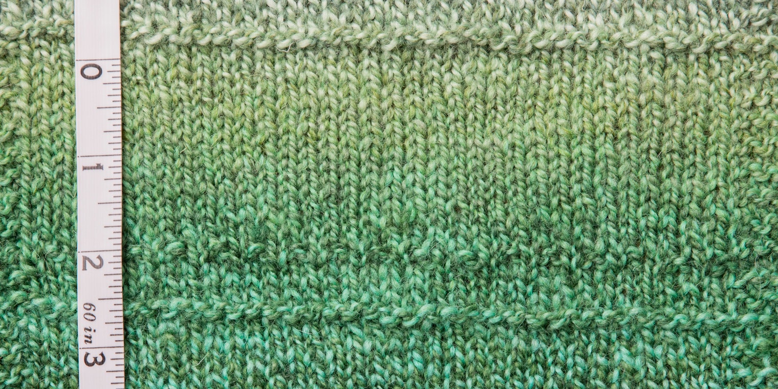 Green marled yarn swatch with tape measure on left side