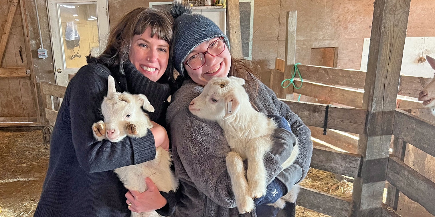 two women holding goats in a barn
