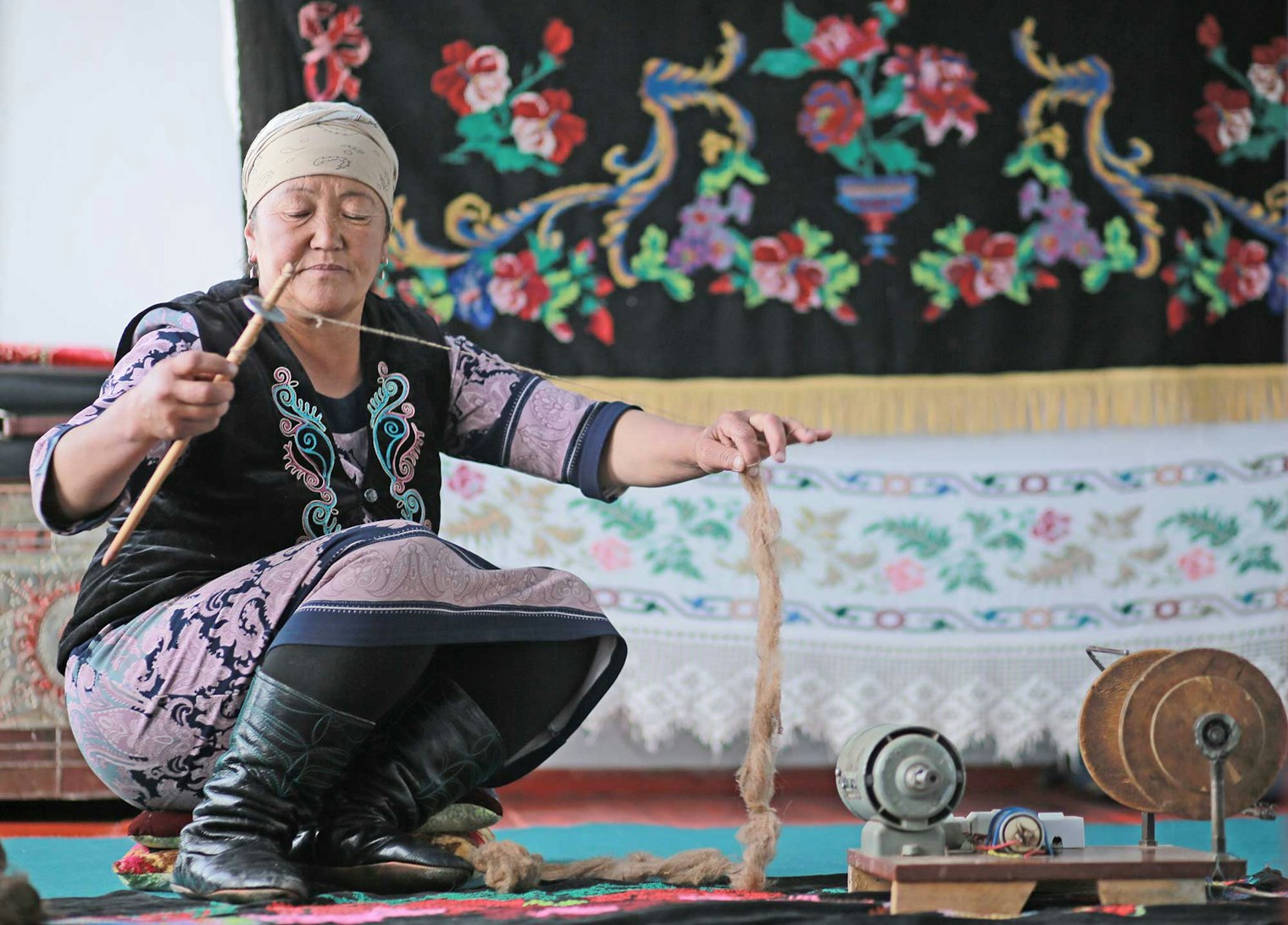 Kyrgyz woman spinning in front of a tapestry she embroidered for her wedding trousseau.