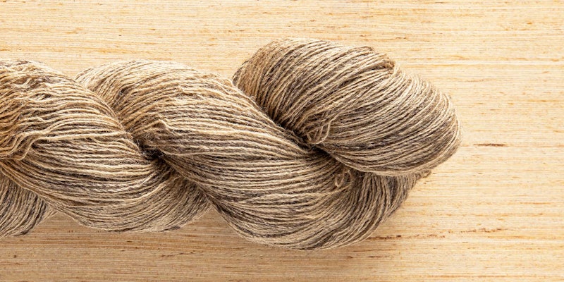 A tan skein of yarn rests on a wooden surface.