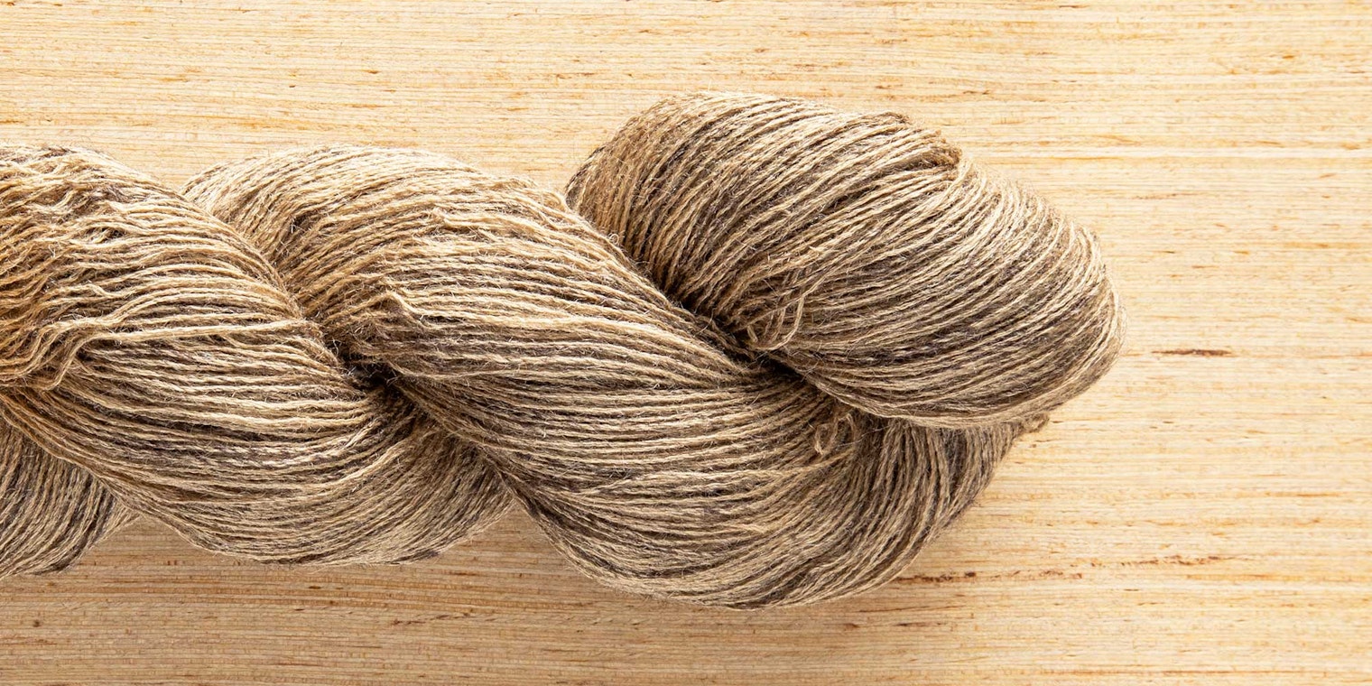 A tan skein of yarn rests on a wooden surface.