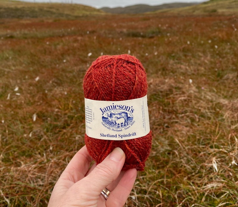 Rust-red skein of yarn against autumn Shetland landscape