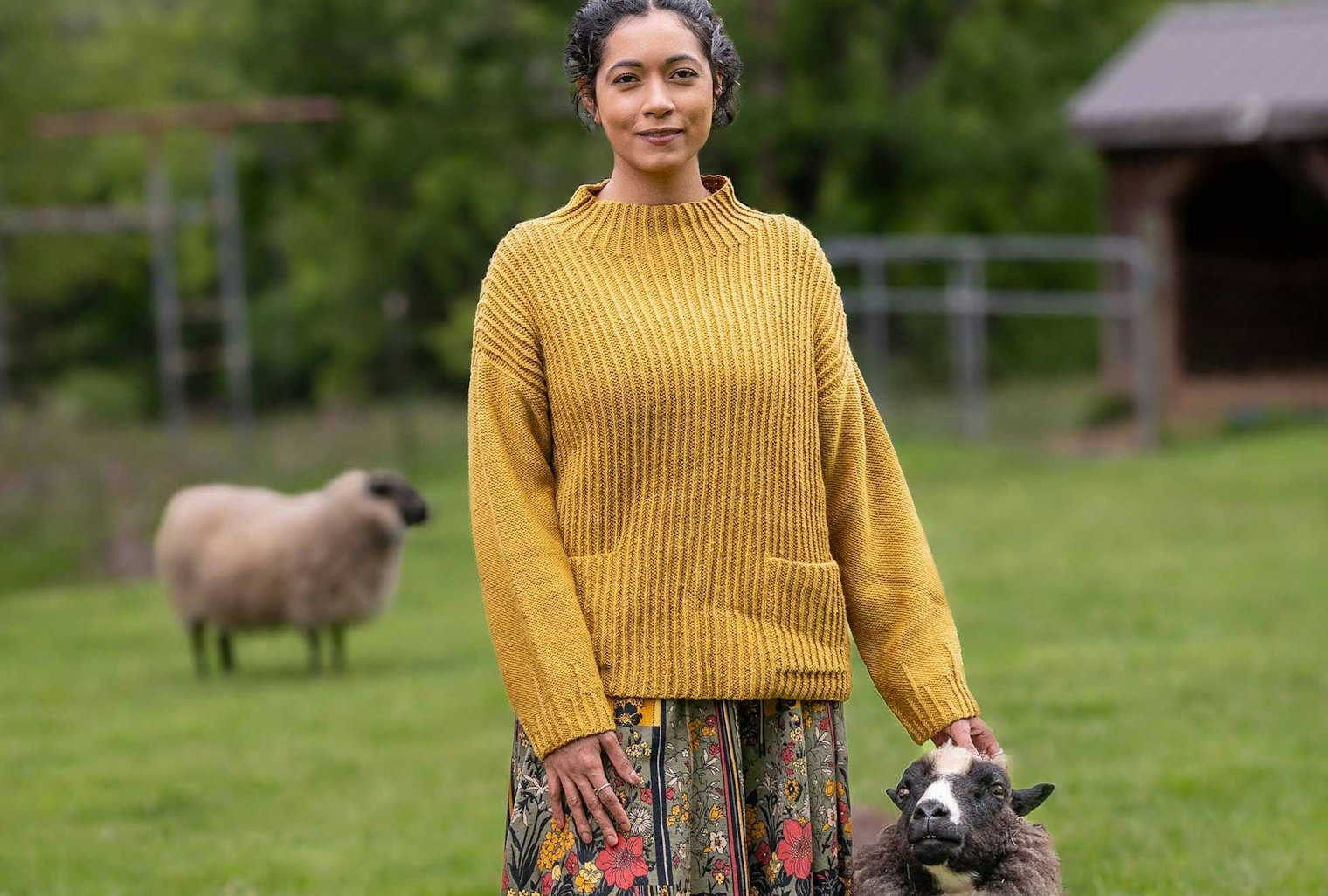 Woman wearing golden yellow knitted sweater and standing next to a sheep