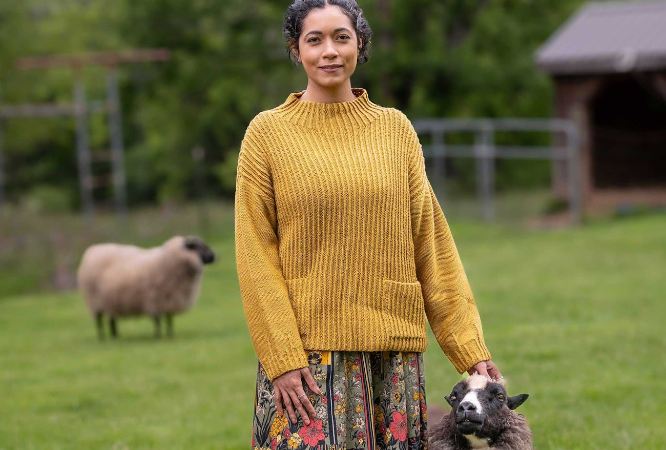 Woman wearing golden yellow knitted sweater and standing next to a sheep