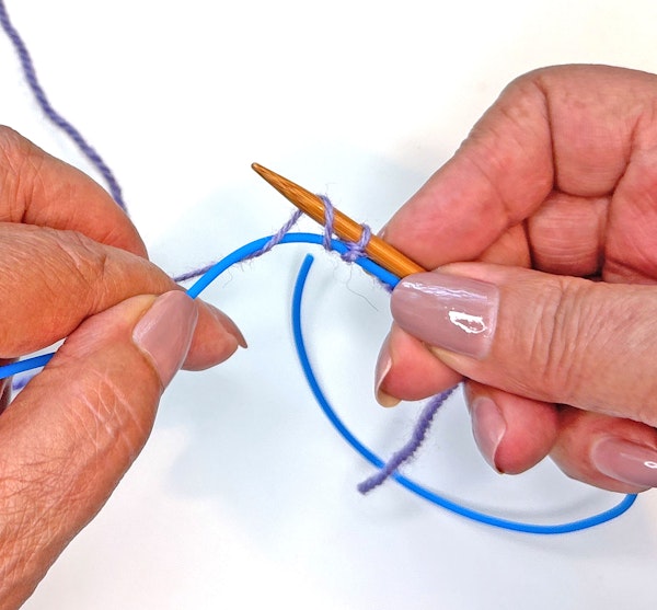 Use the needle to reach under the cord, catch the yarn, and pull up a loop.