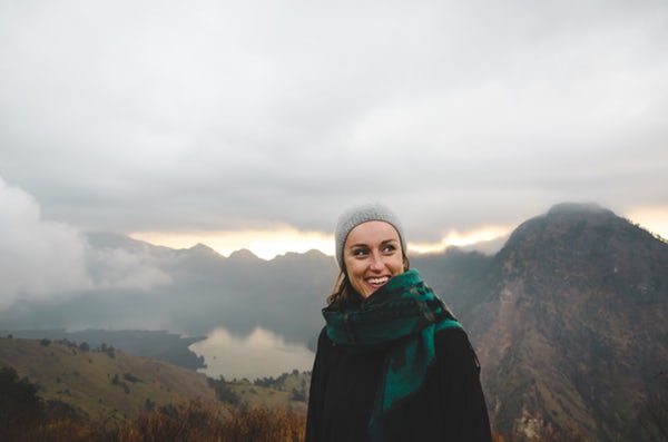 Girl wearing a scarf and hat hiking a tall mountain with clouds.