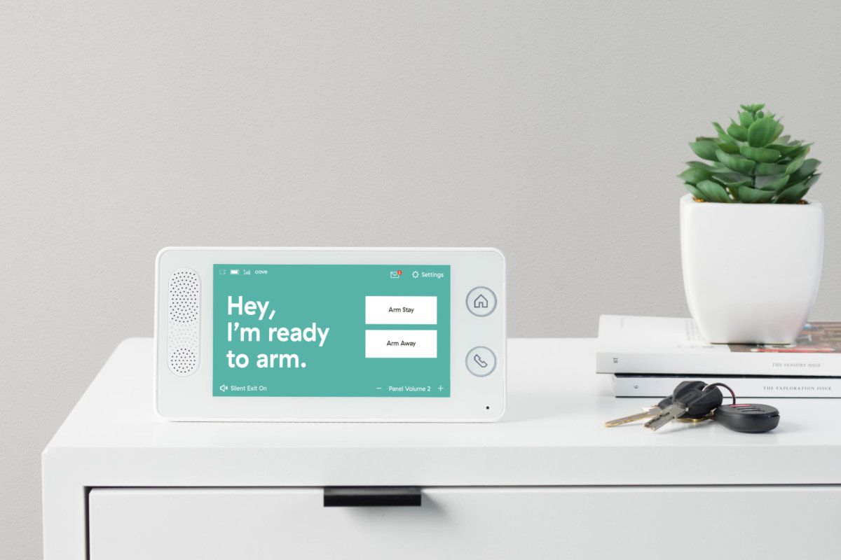 Apartment security device. It's an alarm panel on a desk near a plant, keys and books.