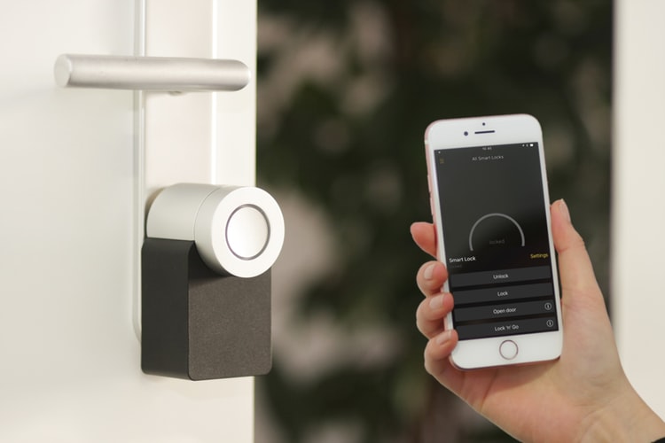 Smart Lock mounted on an open door. Person's hand holding out phone with app to control the lock.