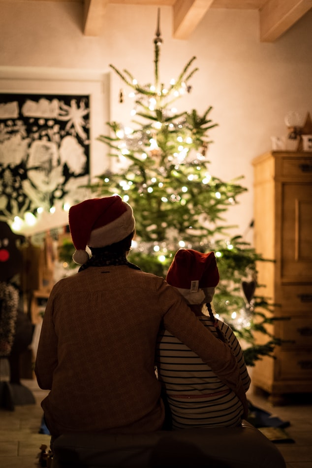 couple sitting in-front of lit Christmas tree 