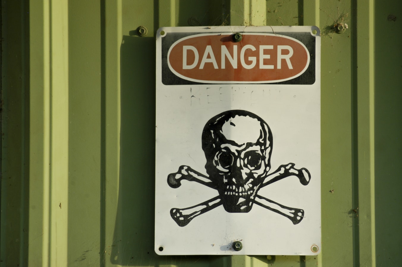 Danger sign with skull and crossbones on a green metal wall.