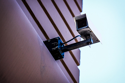 Boxy motion sensor camera mounted on side of a wall of a building with lot's of lines on it.