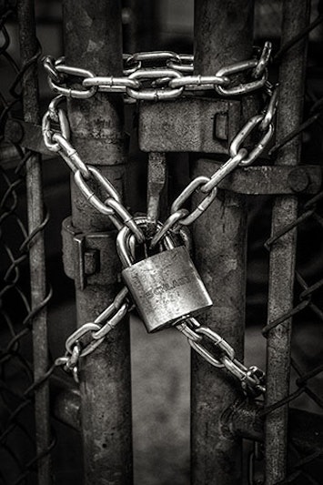 Fence locked with chain for home perimeter security. The filter on the photo makes everything look dark and gray.