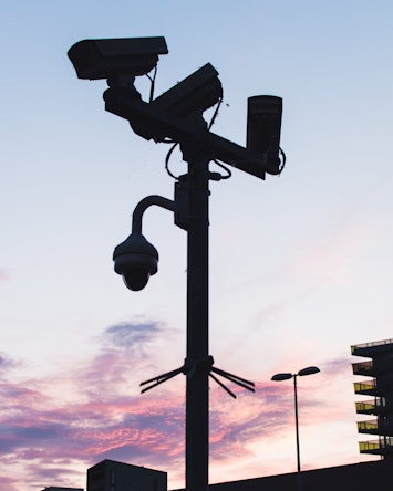 Pole with several different types of cameras mounted on it. The cameras are silhouetted by the setting sun. 