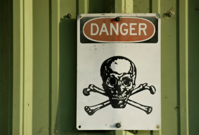 Danger sign with skull and crossbones on a green metal wall.