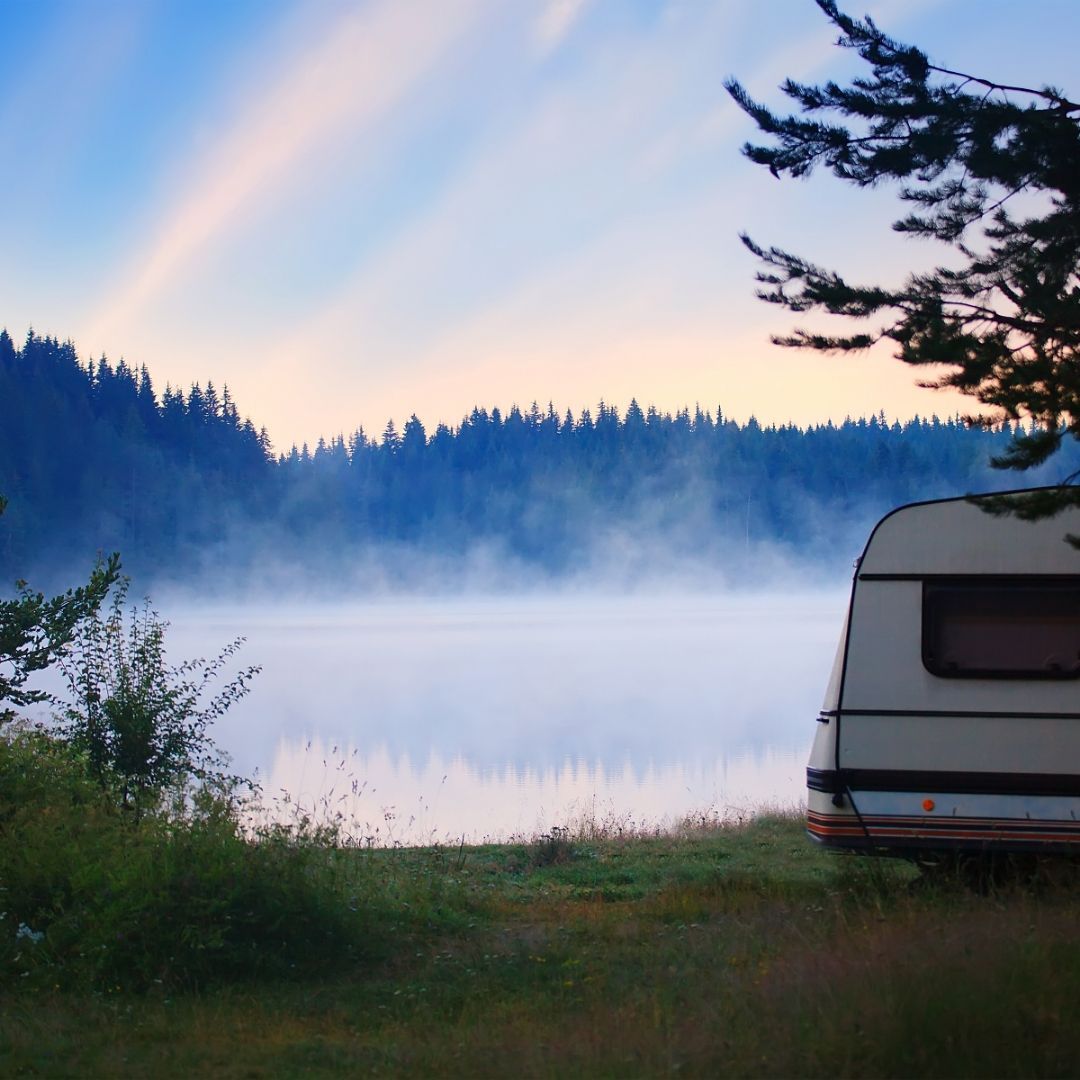 Camper parked next to a steaming lake surrounded by a thick forest of trees.