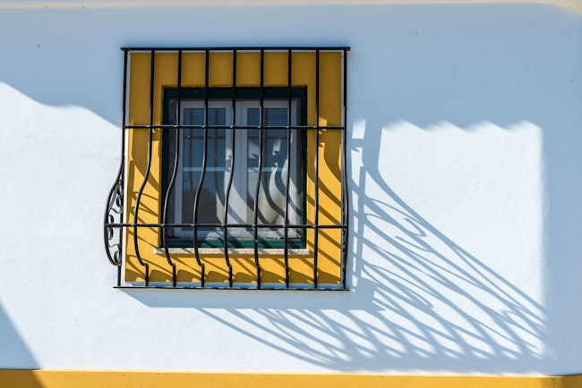 window with a square of yellow paint around it covered by tasteful thin black window bars
