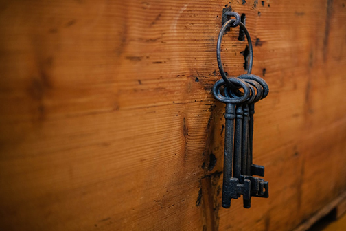 Old fashioned ring of black keys hung on a small hook key holder jutting out of a wood wall. 