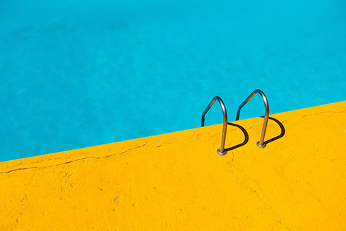 Crystal clear Pool With Yellow Pool Deck and metal stairs attached to pool deck going into the pool.