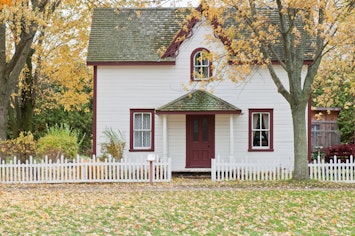 Small House in Autumn with a leaf covered yard and a white picket fence.