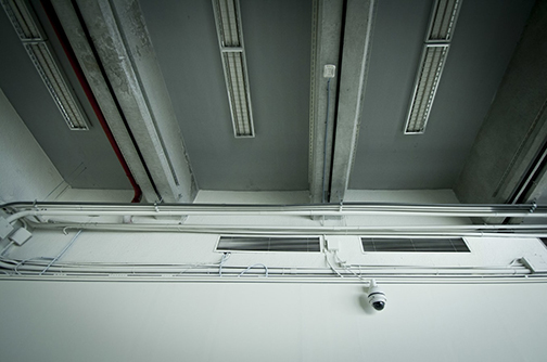 Security Camera on a White Wall. The camera is looking up at the camera and the dingy roof of the room.