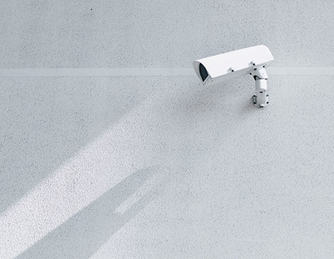 White Security Camera on White Wall. The colors of the photo have been muted to be more gray and white.