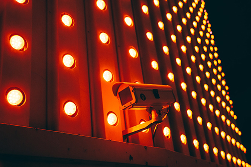 Security camera is illuminated by a wall of round orange lights behind it. 