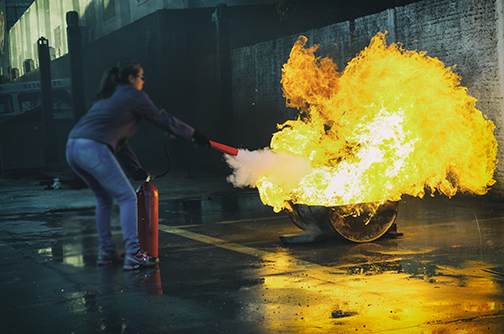 Woman Wearing Goggles Putting out Large Fire With an Extinguisher 