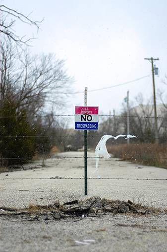 No Trespassing Sign on a post stuck into the dirt and attached to a  barbed wire fence in winter.