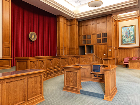 Court room where unlawful entry and trespassing would be tried. Walls made of wood. Old style painting of a man on the wall. 