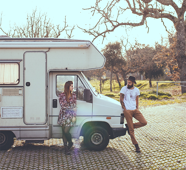 Woman and Man Standing in front of an RV looking loving at each other on a sunny day.
