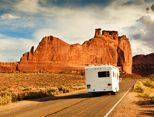 White RV Driving Through a Red Rock Desert. Scattered Clouds in the Sky.