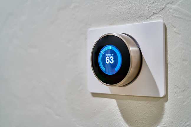 Thermostat mounted on white wall. Blue display of the current temperature.