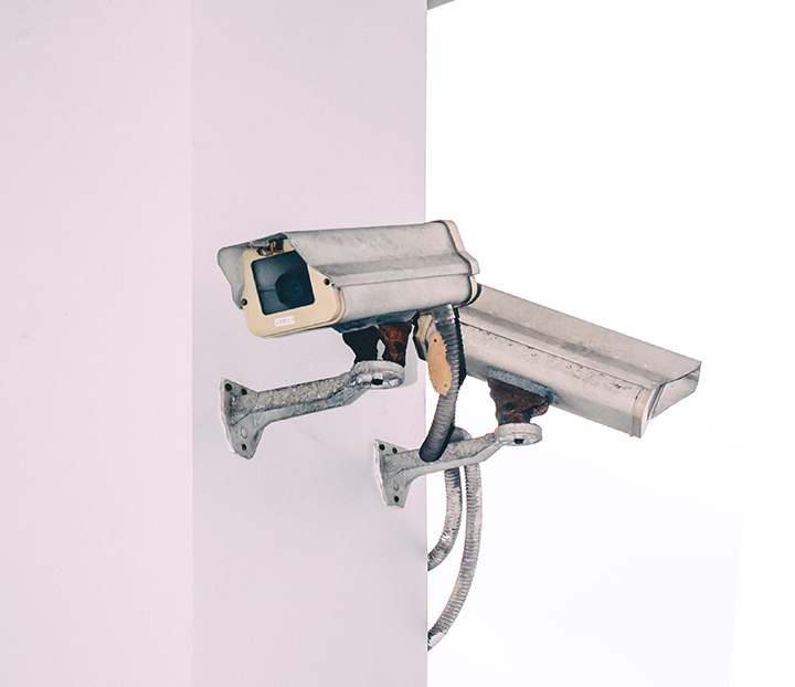 Twin motion detector cameras mounted to the side of a white wall.