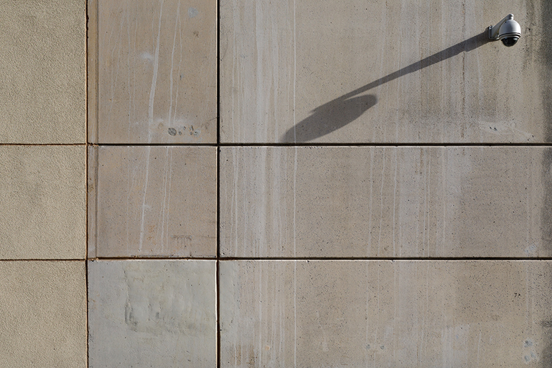 A dome camera casting a long shadow on a concrete wall