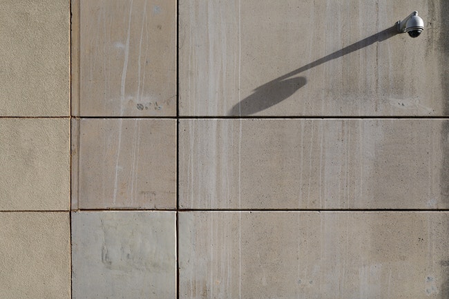A dome camera casting a long shadow on a concrete wall