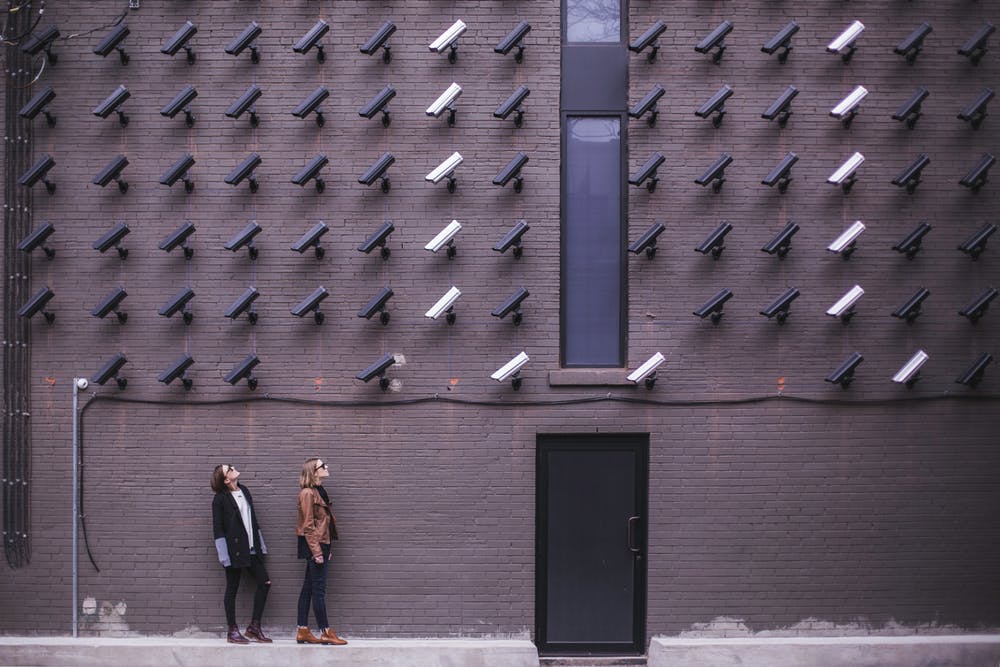 Two people stare up at 50 security cameras all mounted to a wall and all pointing towards them