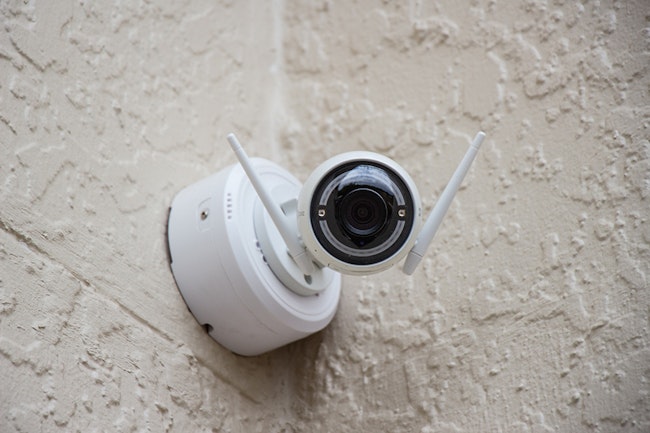 White Cheap Security Camera at corner of tan walls.